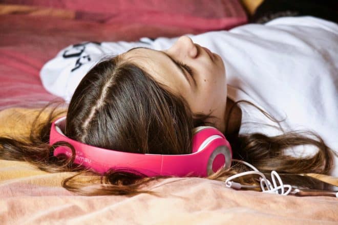 a girl wearing over ear headphones, lying down on a rug or blanket; shotat an angle from behind her head, but likely sleeping.